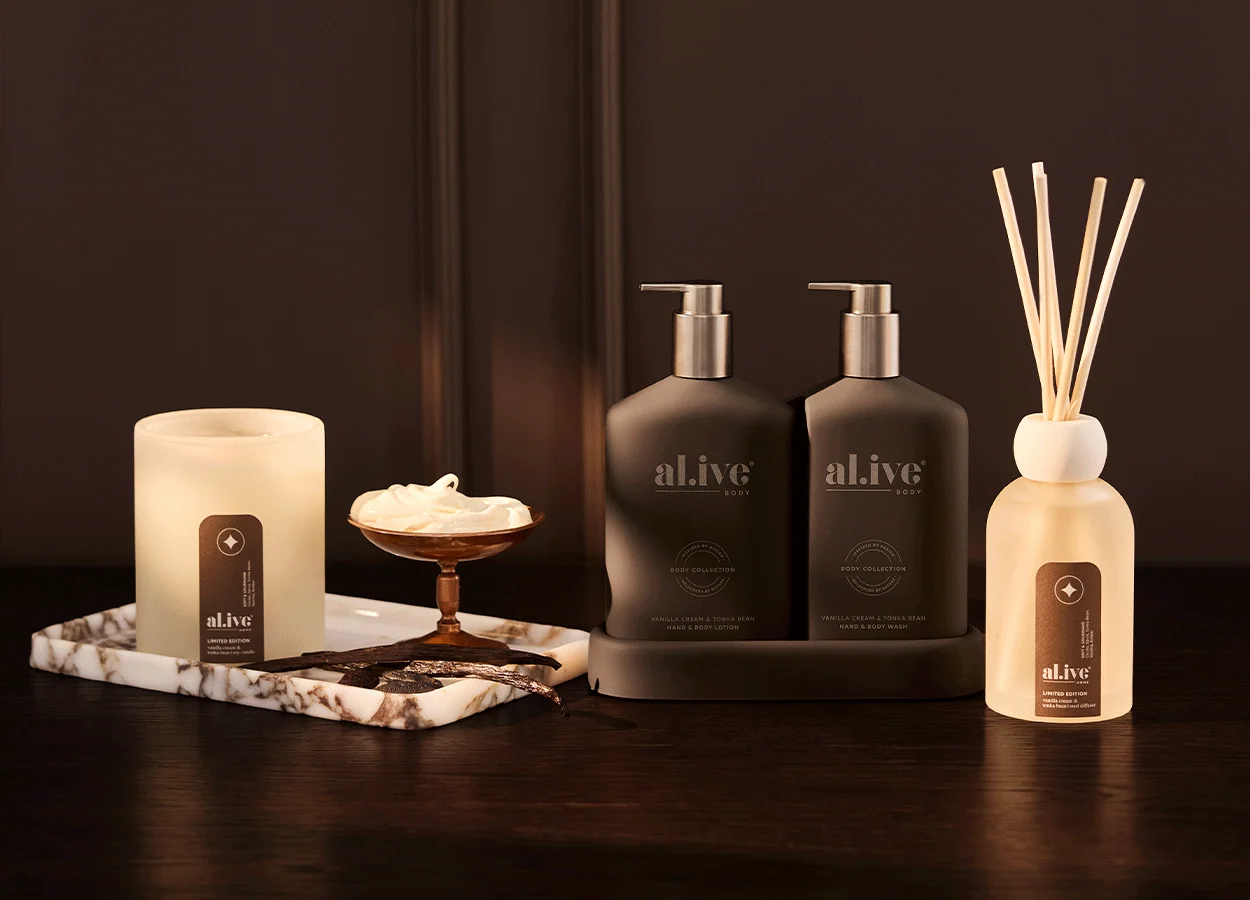 al.ive limited edition vanilla cream and tonka bean candle, hand and body wash and lotion, and reed diffuser on a dark timber table